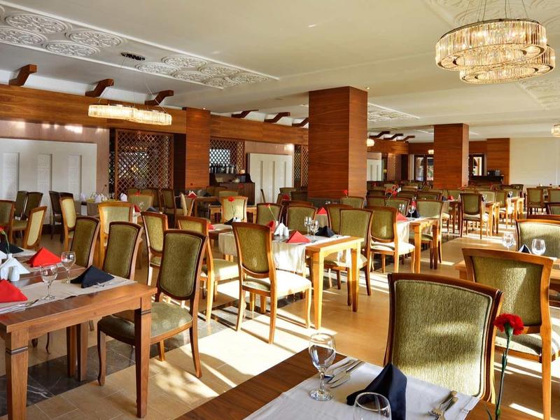 Spacious hotel restaurant with wooden furniture, green chairs, and neatly set tables.