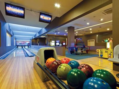 Eine Bowlingbahn mit bunten Bowlingkugeln im Vordergrund und beleuchteten Bahnen im Hintergrund.