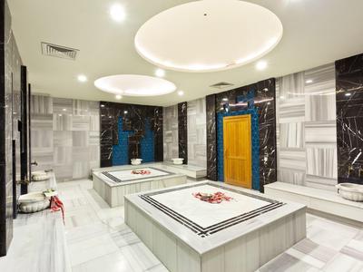 Moderner türkischer Hamam mit weißen Marmorplatten, großen beheizten Liegen und indirektem Licht.