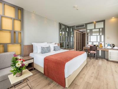 Helles, modernes Schlafzimmer mit großem Bett, Holzboden und Sitzbereich mit Tisch und Blumen.