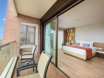 Modernes Hotelzimmer mit Bett, Glas-Schiebetür und Balkon mit Stühlen und Tisch.