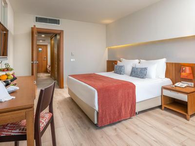 Modernes Hotelzimmer mit Doppelbett, Holzmöbeln, Schreibtisch und warmweißer Beleuchtung.