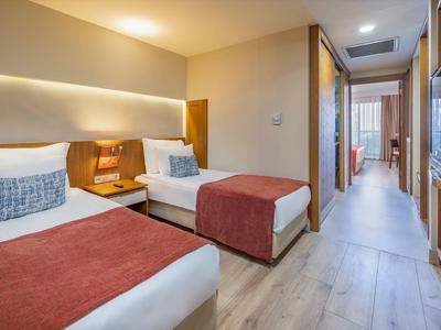 Hotelzimmer mit zwei Einzelbetten, roten Decken, Holzmöbeln und hellem Laminatboden.