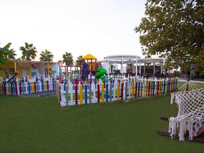 Ein bunter Spielplatz mit Klettergerüsten, umgeben von einem farbenfrohen Zaun und grüner Rasenfläche.