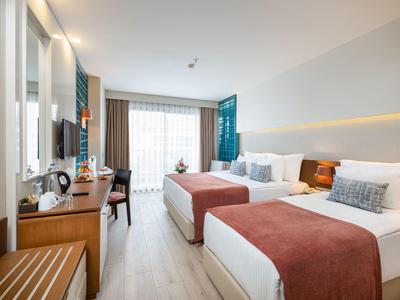 Modern eingerichtetes Hotelzimmer mit zwei Betten, Holzmöbeln und großem Fenster mit Vorhängen.