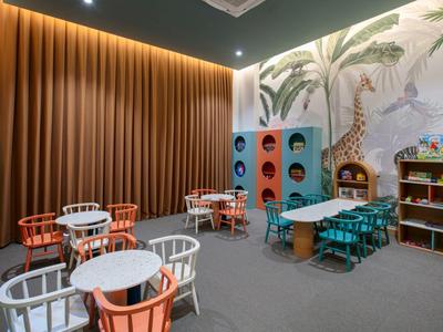 Moderner Kinderspielbereich mit Tischen, Stühlen und farbenfrohen Spielstrukturen in einem Hotel.