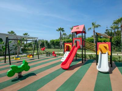 Spielplatz mit bunten Rutschen und Schaukeln in einem sonnigen Hotelgarten.