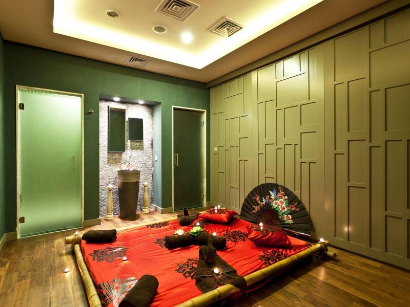 Sala spa con decorazioni asiatiche, tappeto rosso, ventaglio e pareti verdi strutturate.