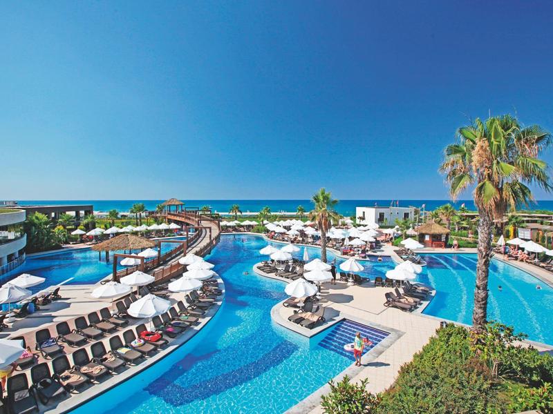 Piscina dell'hotel con lettini, ombrelloni, palme e vista sul mare.