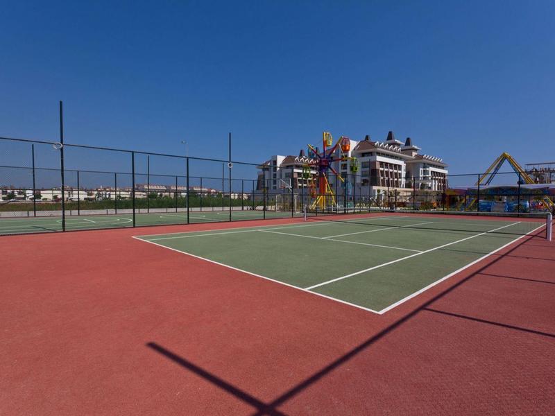 Campo da tennis all'aperto vicino a un complesso alberghiero sotto un cielo azzurro.