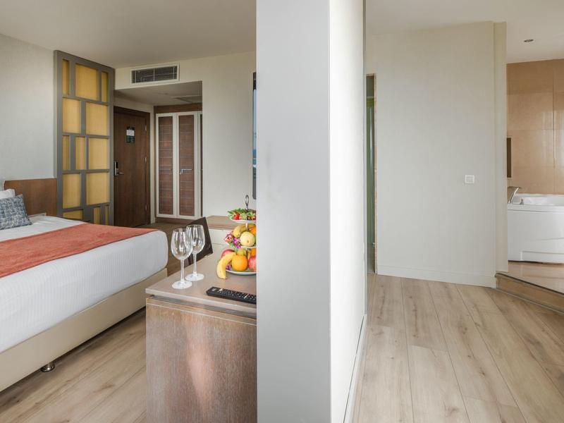 Camera d'hotel moderna con letto e bagno con vasca idromassaggio separati da una parete.