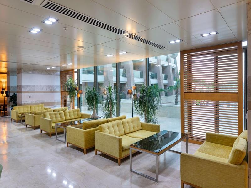 Atrio luminoso con divani gialli e grandi finestre che si affacciano su un giardino interno.