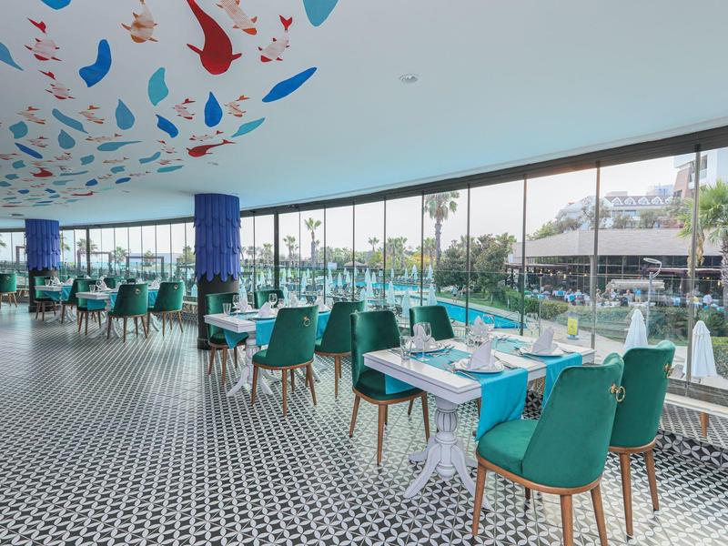 Ristorante moderno con ampie finestre, sedie verdi e decorazioni colorate sul soffitto.