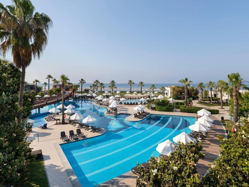 Piscina d'hotel con lettini, ombrelloni bianchi e vista sul mare.