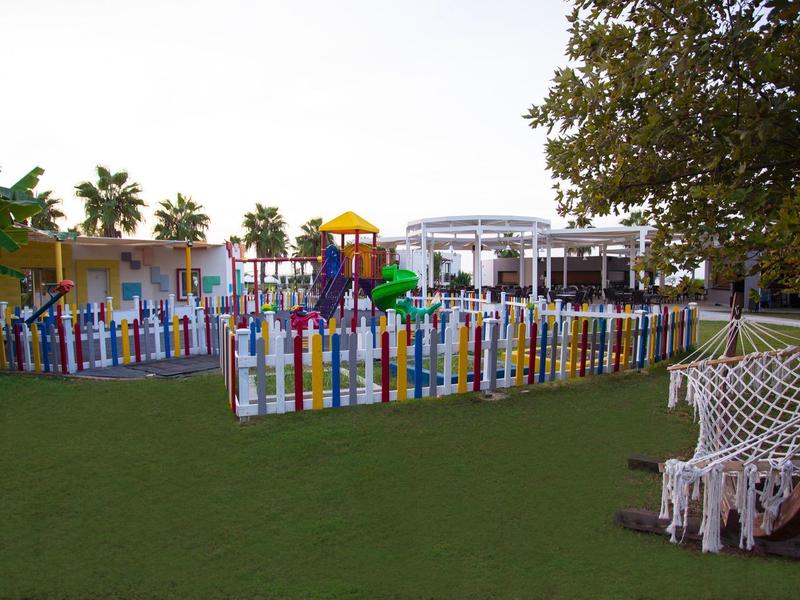 Area giochi colorata recintata da una staccionata multicolore in uno spazio esterno verde.