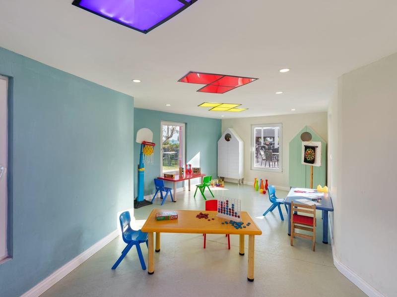 Sala giochi luminosa con tavoli, sedie colorate e luci vivaci sul soffitto.