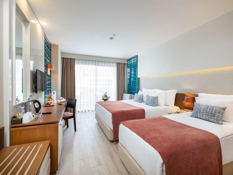 Camera d'albergo luminosa con due letti, scrivania, TV e finestra panoramica.