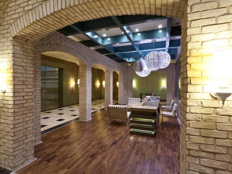 Salone d'albergo con muri di mattoni e soffitto con travi e lampade appese.