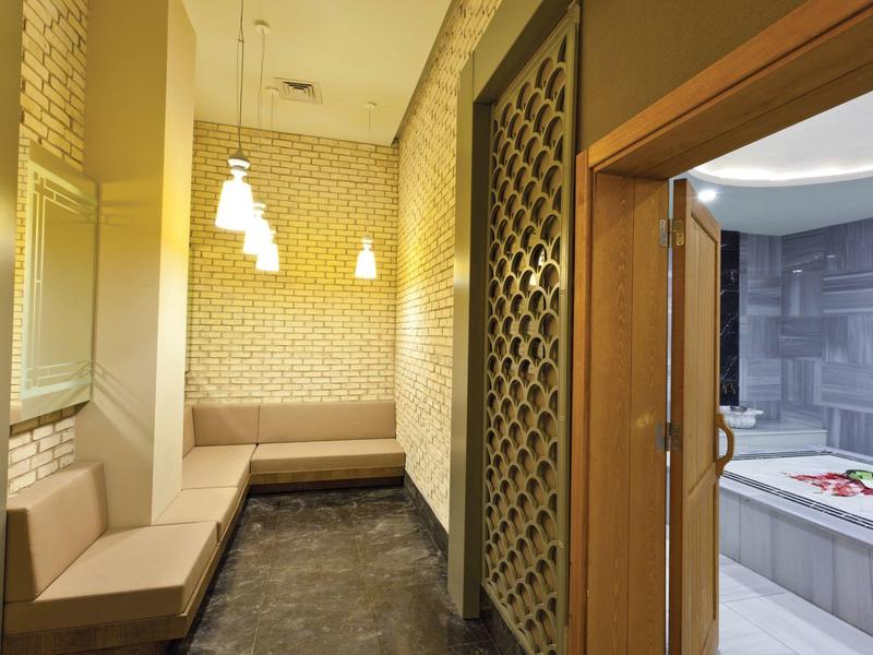 Sala spa con panca beige, luci sospese e ingresso a una vasca idromassaggio.