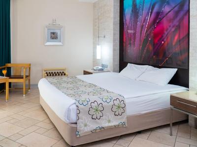 Modernes Schlafzimmer mit großem Bett, buntem Wandbild, Holzmöbeln und hellem Fliesenboden.