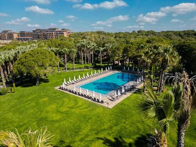 Duży basen na świeżym powietrzu z leżakami i parasolami pośród zielonych trawników i palm.