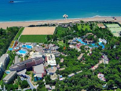 Luftaufnahme einer Küstenregion mit Hotelanlagen, grünen Gärten und einem Sandstrand am blauen Meer.