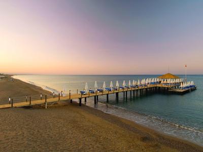 Holzsteg mit weißen Sonnenschirmen am ruhigen Meer bei Sonnenuntergang und blauem Himmel.