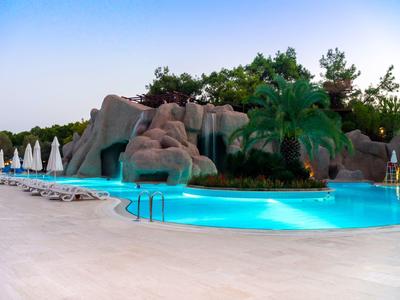 Schwimmbad mit klarem blauen Wasser, Felsen, Palmen und geschlossenen weißen Sonnenschirmen.