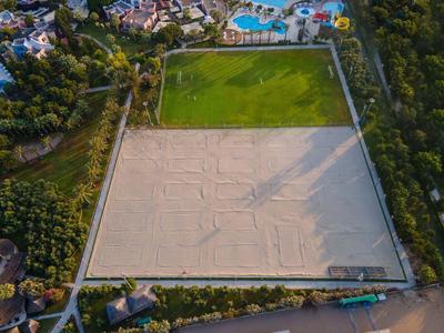 Großes rechteckiges Gelände mit Sandfläche, Rasenfeld und umgeben von Bäumen und Gebäuden.