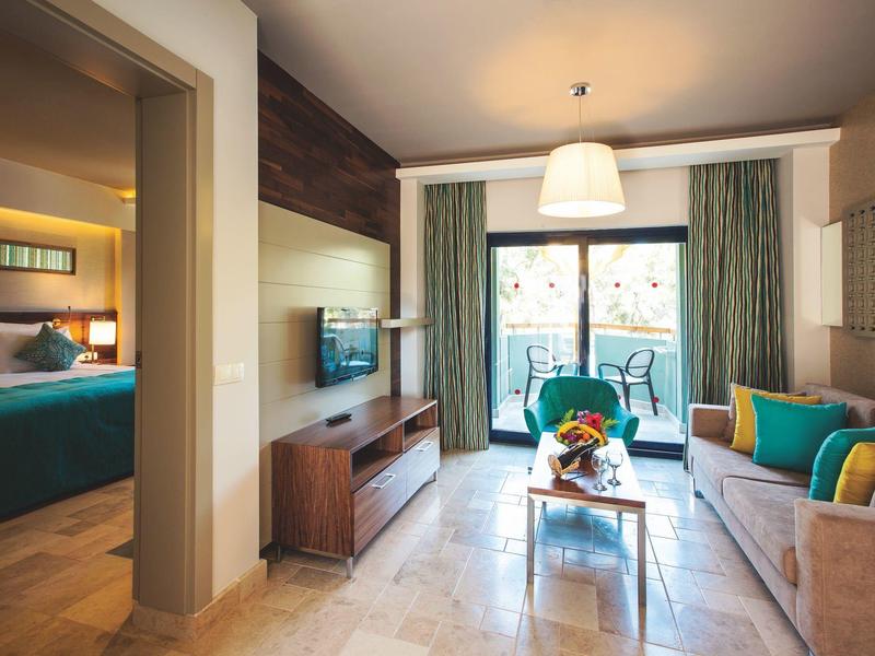 Modernes Wohnzimmer mit bequemen Sofas, Glastisch, TV und Zugang zu einem Balkon mit Stühlen.