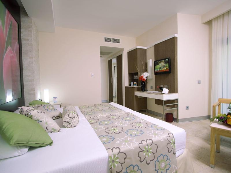 Helles Schlafzimmer mit großem Bett, grün-weißer Bettwäsche und modernem Schreibtisch am Fenster.