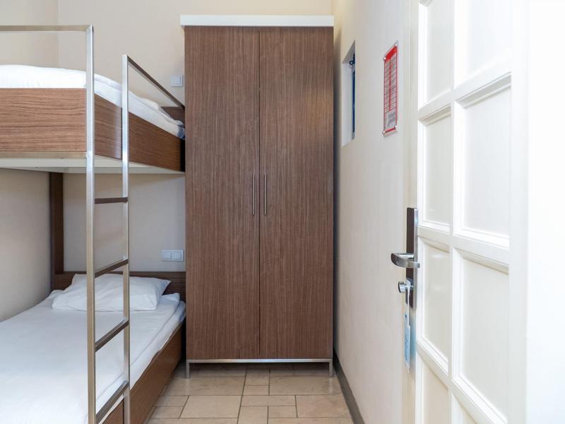 Enges Zimmer mit Etagenbett, braunem Schrank, weißer Tür und beigem Fliesenboden.