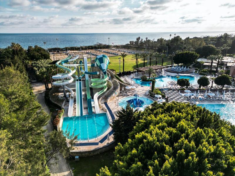 Freizeitpark mit Wasserrutschen und Pools an der Küste, umgeben von Bäumen und Rasenflächen.