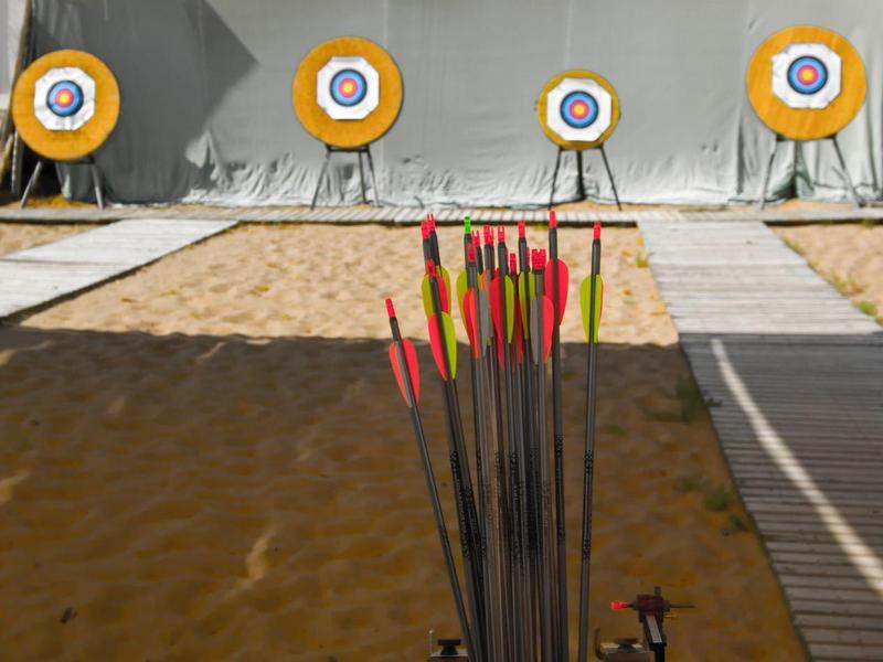 Bogenschießplatz mit Pfeilen, Bogen und vier Zielscheiben vor einer weißen Wand.