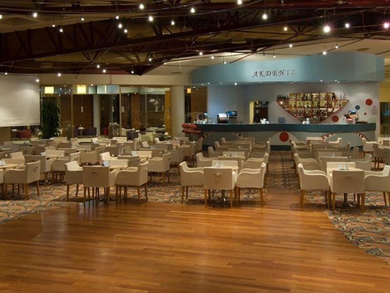 Großer Veranstaltungsraum mit Holzboden, Stuhlreihen, Deckenbeleuchtung und Buffetbereich hinten.