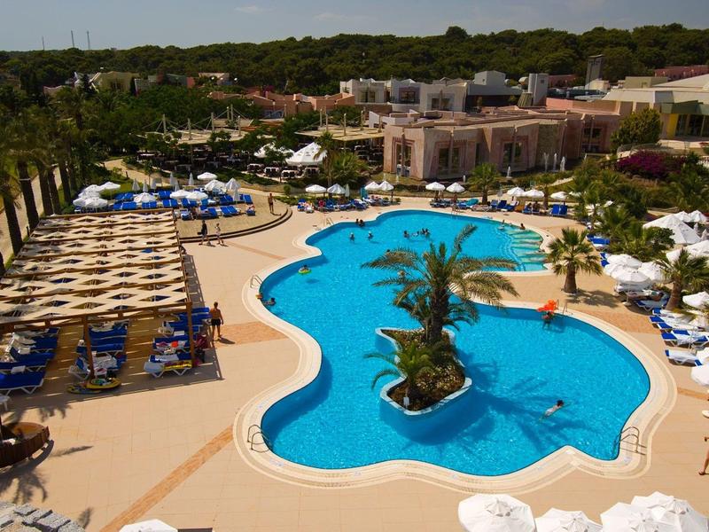 Großer, unregelmäßig geformter Pool mit Palmeninsel, umgeben von Liegestühlen und Sonnenschirmen.