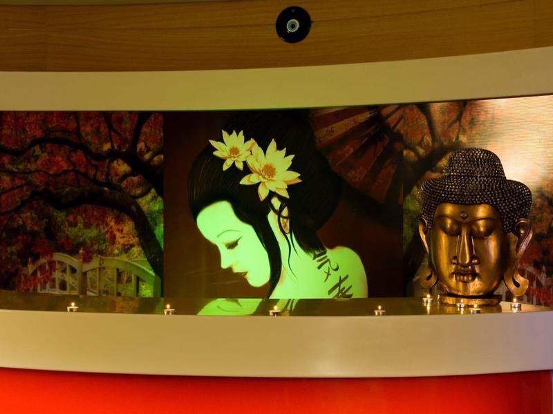 Ein hell erleuchtetes Gemälde mit grüner Silhouette und gelben Blumen, flankiert von zwei goldenen Statuen.