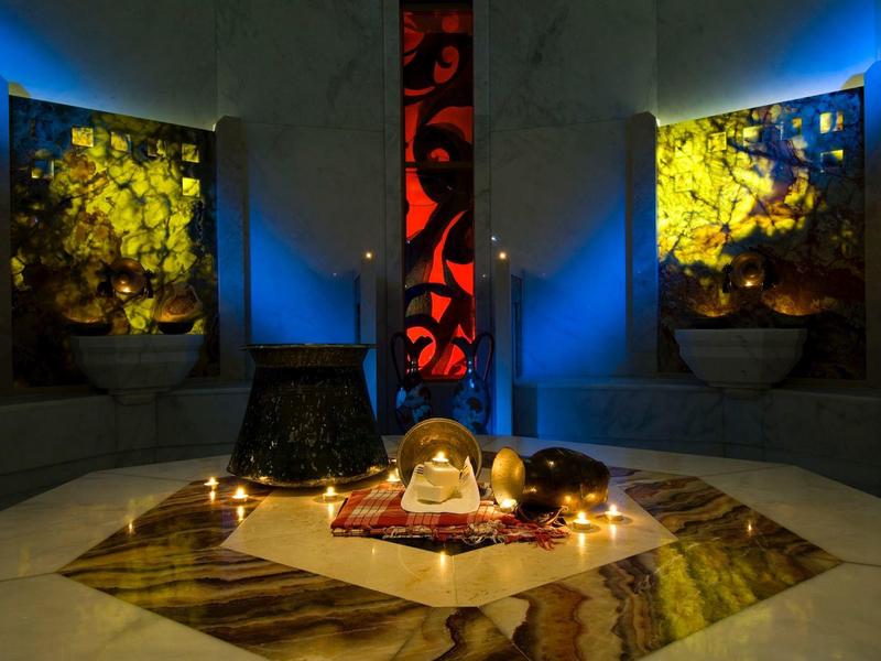 Dimmer Raum mit Marmorboden, farbigen Glasbildern und leuchtenden Glasobjekten auf einem Teppich.