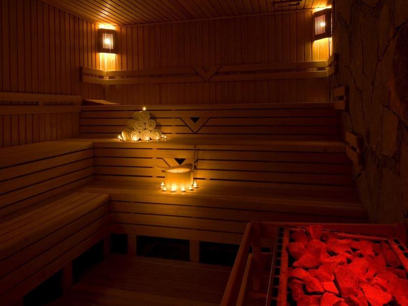 Sauna mit holzverkleideten Wänden, mehrstufigen Holzbänken, warmem Licht und roten Heizsteinen.