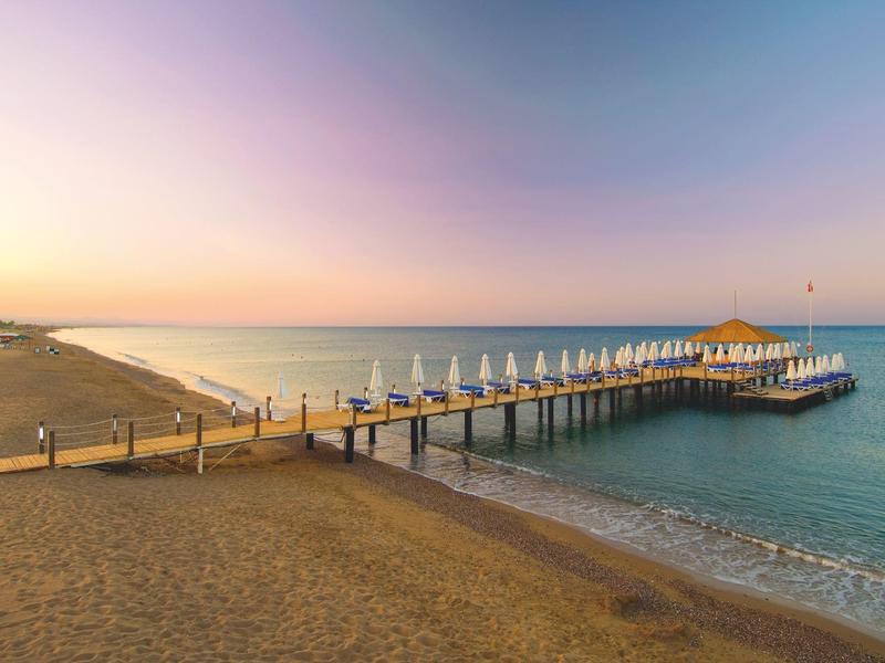 Langer Holzsteg mit weißen Sonnenschirmen am ruhigen Meer unter sanftem Abendhimmel.