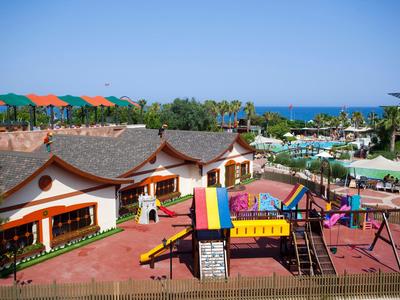 Colorful playground next to traditional-style buildings and pools with umbrellas by the sea.