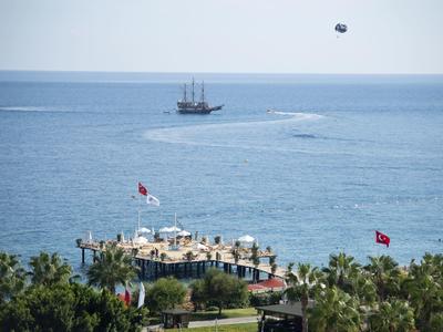 Seaside resort with a deck, flags, and a sailboat on calm blue water.