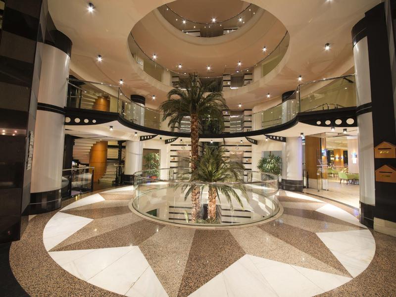 Spacious hotel lobby with circular patterned floor, central palm tree, and curved balcony.
