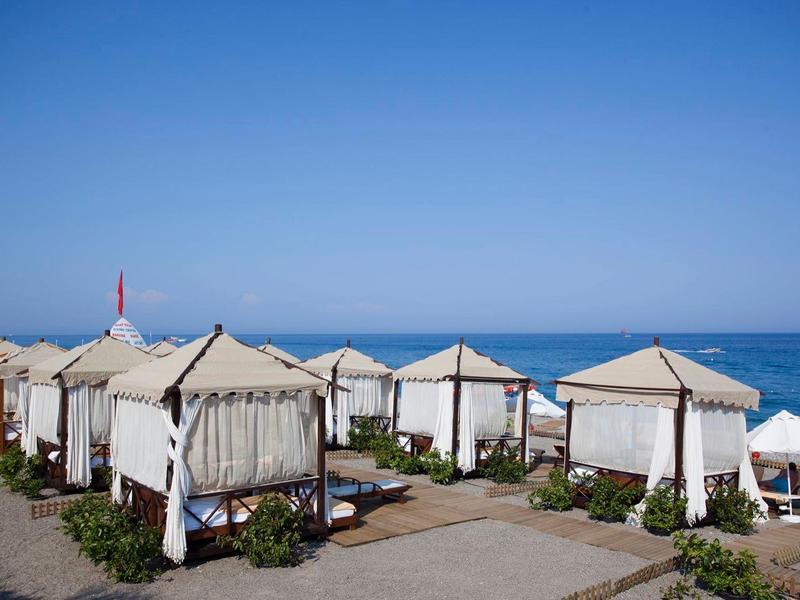 Beachside cabanas with white curtains near the sea under a clear blue sky.