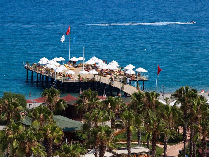 Wooden pier with umbrellas and seating extending into the blue ocean, surrounded by palm trees.