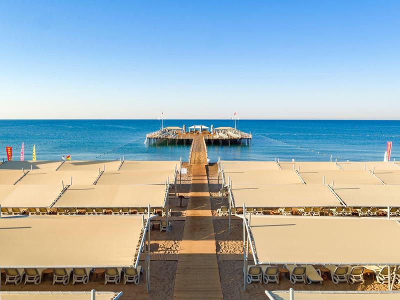 Symmetrical beach pier extending into calm blue sea under clear sky.