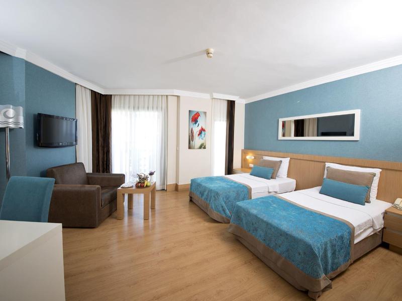 Hotel room with two single beds, blue accents, a sofa, and natural light from a window.