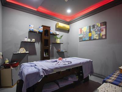 Stanza massaggi tranquilla con lettino beige, quadri colorati e illuminazione rossa sul soffitto.