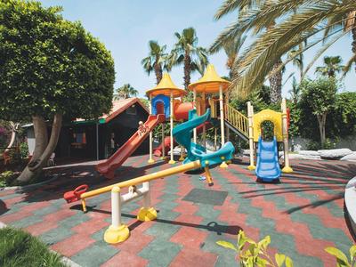 Parco giochi colorato per bambini con scivoli e altalene in un giardino tropicale.