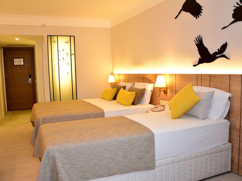 Camera d'hotel con due letti, colori neutri e decorazione murale con uccelli